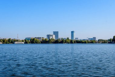 Romanya 'nın Bükreş kentindeki Herastrau Park' ta güneşli bir sonbahar gününde göl kenarında çok sayıda büyük yeşil ve yaşlı ağaçla manzara