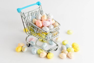 Çikolata kaplı Paskalya yumurtaları beyaz bir masada izole edilmiş küçük bir süpermarket alışveriş arabasında. 