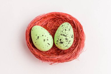 İki yeşil renkli paskalya yumurtası kırmızı kırsal bir sepette beyaz bir masada izole edilmiş.