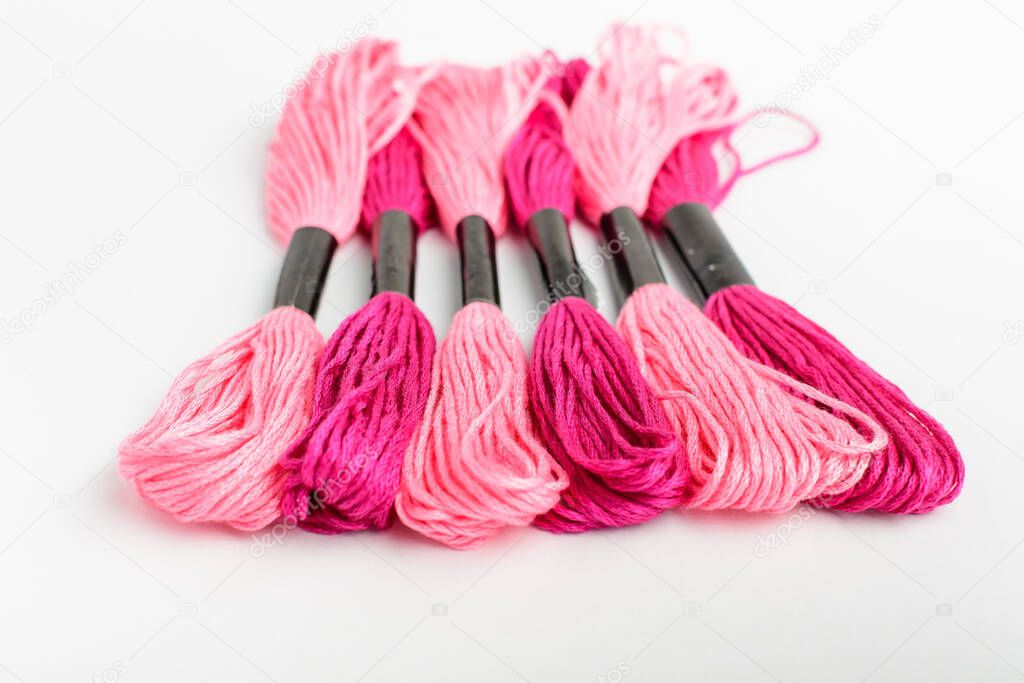 Many mixed vivid pink sewing threads for embroidery isolated on a white table, top view or flat lay of textile materials