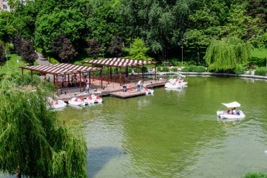 Bükreş, Romanya - 29 Mayıs 2021: Romanya 'nın Bükreş kentindeki Moghioros Parkı olarak da bilinen Drumul Taberei Parkı' ndaki göl ve canlı yeşil ağaçlarla manzara bulutlu bir yaz gününde