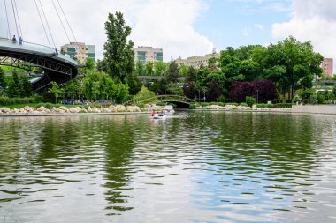 Bükreş, Romanya - 29 Mayıs 2021: Romanya 'nın Bükreş kentindeki Moghioros Parkı olarak da bilinen Drumul Taberei Parkı' ndaki göl ve canlı yeşil ağaçlarla manzara bulutlu bir yaz gününde