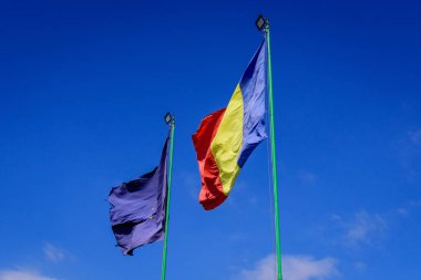 Avrupa Birliği ve Rumen ulusal bayrakları güneşli bir bahar gününde bulutlu mavi gökyüzüne doğru rüzgarda dalgalanıyor