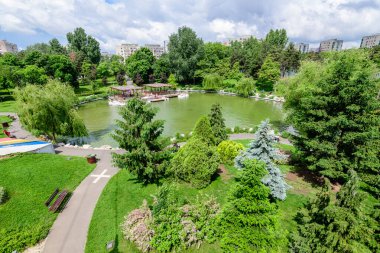 Romanya 'nın Bükreş kentindeki Moghioros Parkı olarak da bilinen Drumul Taberei Parkı' nda (Parcul Drumul Taberei), bulutlu bir yaz gününde göl ve canlı yeşil ağaçlarla çevrili manzara