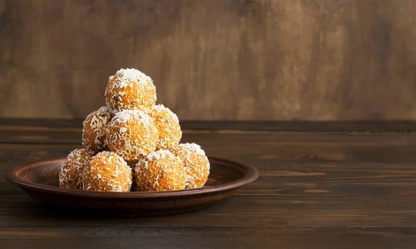 Homemade energy balls of raw carrots, dates, nuts and coconut on a brown wooden background. A healthy sugar-free dessert for adults and children. Copy space.