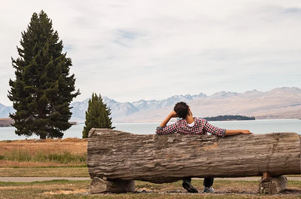 Mujer sentada en un banco de madera junto a un lago Imagen de archivo