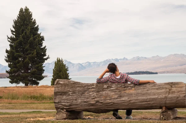 Mujer sentada en un banco de madera junto a un lago Imágenes de stock libres de derechos