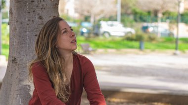 Genç sarışın ahşap ağaç altında oturur.