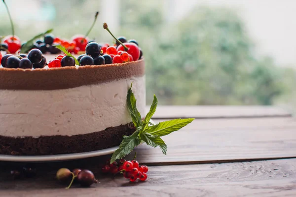 Mousse cake with berries on a wooden table. Chocolate cream cake with currants and cherries. Berry cake for birthday, wedding and other holidays.