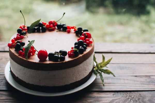 Mousse cake with berries on a wooden table. Chocolate cream cake with currants and cherries. Berry cake for birthday, wedding and other holidays.