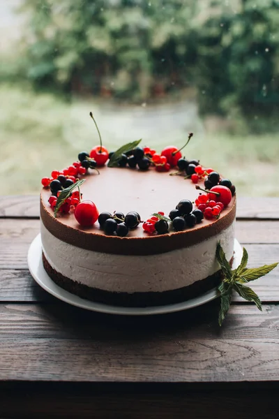 Mousse cake with berries on a wooden table. Chocolate cream cake with currants and cherries. Berry cake for birthday, wedding and other holidays.