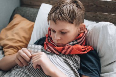 Hasta, grip olmuş genç çocuk yatakta hapşırıyor ve öksürüyor. Hastanın vücut ısısının ölçümü.