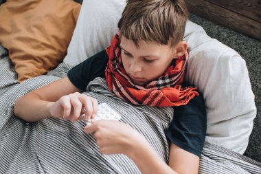 Hasta, grip olmuş genç çocuk yatakta hapşırıyor ve öksürüyor. Hastanın vücut ısısının ölçümü.