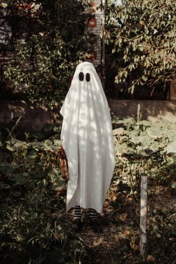 Klasik bir Cadılar Bayramı hayalet kostümü. Çarşaftan yapılmış takım elbise. Parti kostümü giymiş bir çocuk korkutur. Şaka mı şeker mi?. 