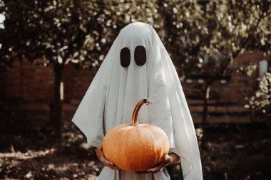 Klasik bir Cadılar Bayramı hayalet kostümü. Çarşaftan yapılmış takım elbise. Parti kostümü giymiş bir çocuk korkutur. Şaka mı şeker mi?. 