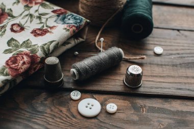 İğne işi konsepti. Çeşitli dikiş aletleri. İğneler, makas, düğmeler, makaralar, farklı renkte iplikler. Aksesuar ve kumaş dikiyorum. Dikiş iplikleri, iğneler, iğneler, ahşap bir arka planda kumaşlar.
