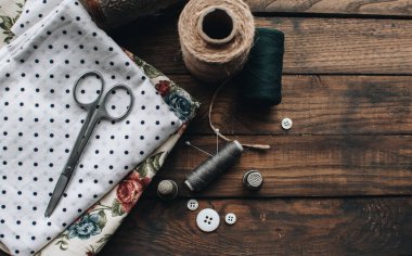 İğne işi konsepti. Çeşitli dikiş aletleri. İğneler, makas, düğmeler, makaralar, farklı renkte iplikler. Aksesuar ve kumaş dikiyorum. Dikiş iplikleri, iğneler, iğneler, ahşap bir arka planda kumaşlar.