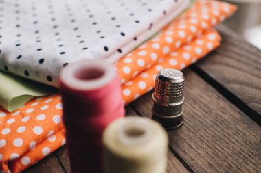 İğne işi konsepti. Çeşitli dikiş aletleri. İğneler, makas, düğmeler, makaralar, farklı renkte iplikler. Aksesuar ve kumaş dikiyorum. Dikiş iplikleri, iğneler, iğneler, ahşap bir arka planda kumaşlar.