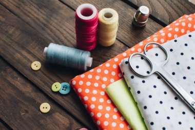 İğne işi konsepti. Çeşitli dikiş aletleri. İğneler, makas, düğmeler, makaralar, farklı renkte iplikler. Aksesuar ve kumaş dikiyorum. Dikiş iplikleri, iğneler, iğneler, ahşap bir arka planda kumaşlar.