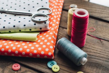 İğne işi konsepti. Çeşitli dikiş aletleri. İğneler, makas, düğmeler, makaralar, farklı renkte iplikler. Aksesuar ve kumaş dikiyorum. Dikiş iplikleri, iğneler, iğneler, ahşap bir arka planda kumaşlar.