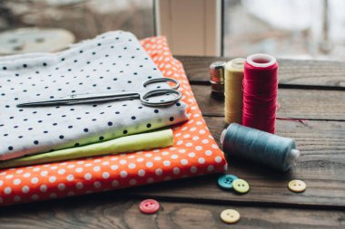 İğne işi konsepti. Çeşitli dikiş aletleri. İğneler, makas, düğmeler, makaralar, farklı renkte iplikler. Aksesuar ve kumaş dikiyorum. Dikiş iplikleri, iğneler, iğneler, ahşap bir arka planda kumaşlar.