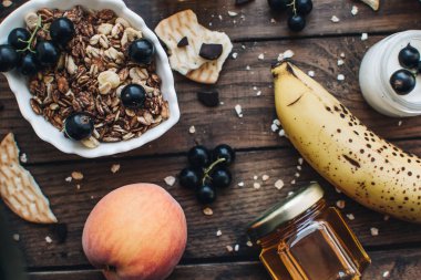 Healthy breakfast ingredients. Homemade granola, oatmeal, yogurt in the bottle, honey, berries and fruits on a wooden background. Morning aesthetics and beautiful layout on a wooden table.	
