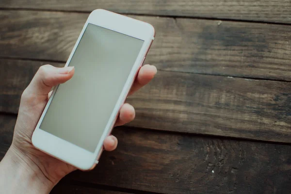 Person holding a phone in a hand on the wooden background. Phone mockup.