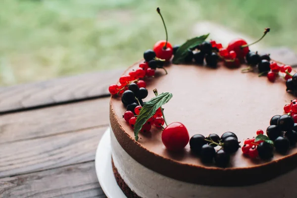 Mousse cake with berries on a wooden table. Chocolate cream cake with currants and cherries. Berry cake for birthday, wedding and other holidays.