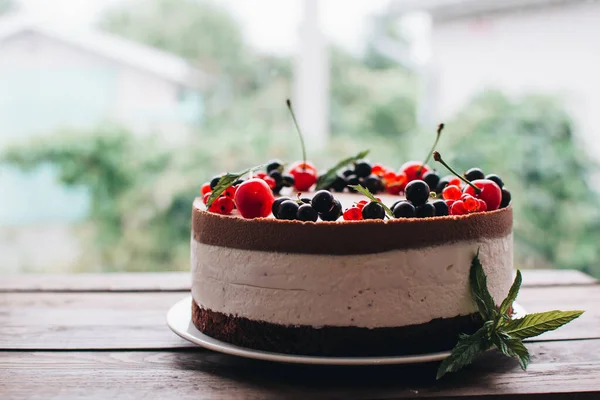 Mousse cake with berries on a wooden table. Chocolate cream cake with currants and cherries. Berry cake for birthday, wedding and other holidays.