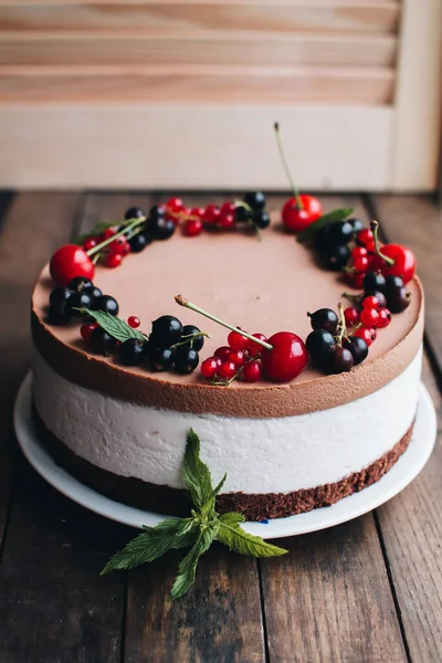 Mousse cake with berries on a wooden table. Chocolate cream cake with currants and cherries. Berry cake for birthday, wedding and other holidays.