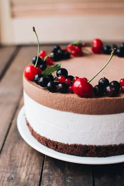 Mousse cake with berries on a wooden table. Chocolate cream cake with currants and cherries. Berry cake for birthday, wedding and other holidays.