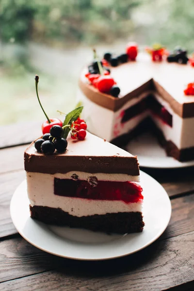 Mousse cake with berries on a wooden table. Chocolate cream cake with currants and cherries. Berry cake for birthday, wedding and other holidays.