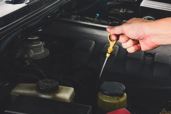 close up auto mechanic\'s hand checks the level of engine oil in a car engine during maintenance