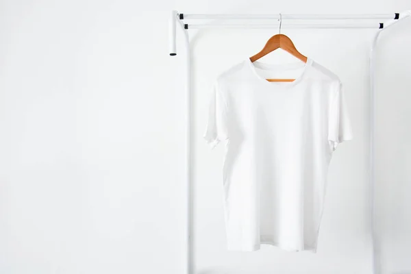 close up of white color t-shirt hanging on wooden clothes hanger on clothing rack over white background, copy space