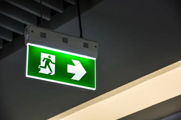 Illuminated green emergency exit sign hanging on ceiling in modern building