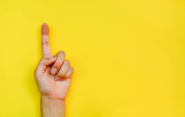 Kahverengi elastik kumaş alçısını kapatır veya kadının işaret parmağına bantla yardım eder sarı arka planda, kopyalama alanında, düz yerde