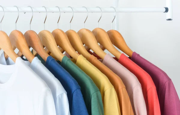 close up collection of colorful t-shirts hanging on wooden clothes hanger in closet or clothing rack over white background, copy space