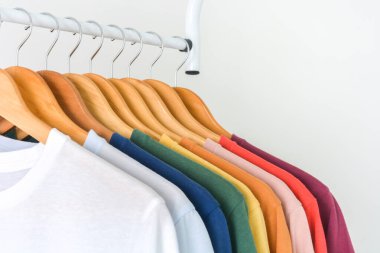 Dolaptaki ahşap elbise askısına asılı renkli tişört koleksiyonunu kapat ya da beyaz arkaplanda elbise askısı, kopyalama alanı