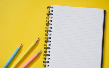 Üzerinde pastel renkli kalemler olan boş çizgili defterlerin üst görünümü kopya alanı olan sarı arka plan, düz yatıyordu