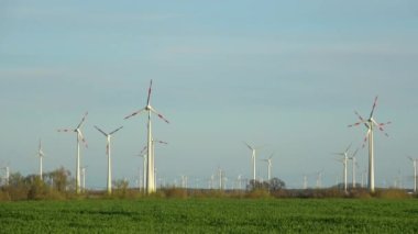 Birçok rüzgar türbini günbatımında bir tarlada durur ve elektrik üretir.