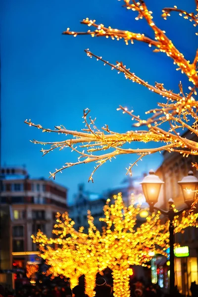 Christmas artificial trees with lights on city streets in the evening