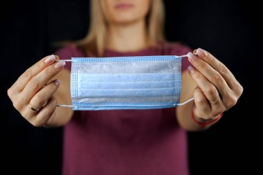 Tek kullanımlık tıbbi maske, siyah arka planda, kadınların elinde.