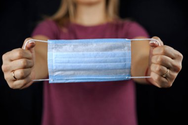 Tek kullanımlık tıbbi maske, siyah arka planda, kadınların elinde.