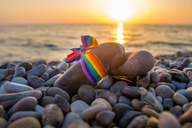Gökkuşağı kurdelesi - Gün batımında deniz kıyısındaki taşların üzerindeki LGBT sembolü