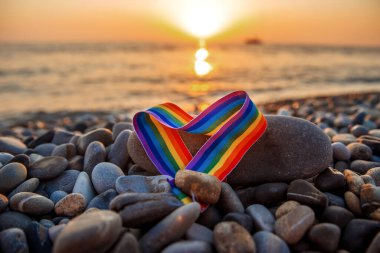 Kalp şeklinde gökkuşağı kurdelesi. Gün batımında deniz kenarındaki taşların üzerindeki LGBT sembolü.