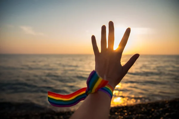 Hand Med Regnbågsband Symbol För Hbt Bakgrunden Havssolnedgång Genom Solens — Stockfoto
