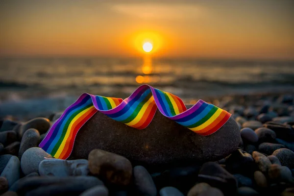 Rainbow ribbon - LGBT symbol on stones on the seashore at sunset