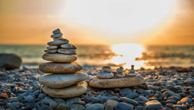 Piramit taşları sahili deniz günbatımının arka planına karşı dengeler.