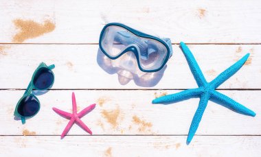 İki yıldız balığı, bir dalış maskesi ve beyaz ahşap arka planda kum serpiştirilmiş güneş gözlüğü. Yaz arkaplanı