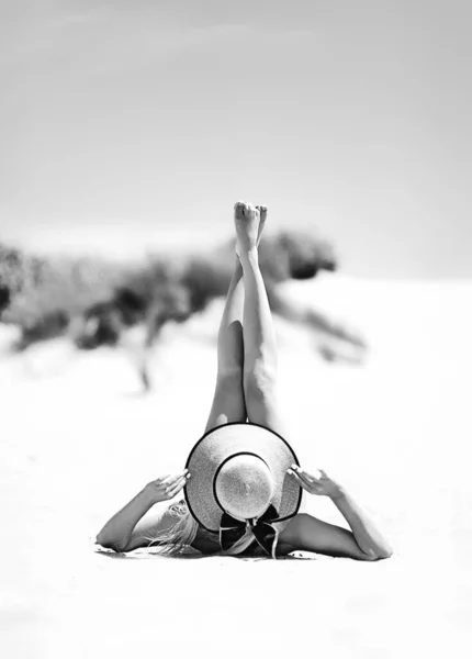 Summer vacation fashion concept - sunbathing woman in sun hat on the beach on the sand